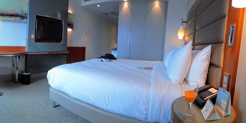 Image of a hotel room with a cosy bed and clean sheets, also a chair and table in the room