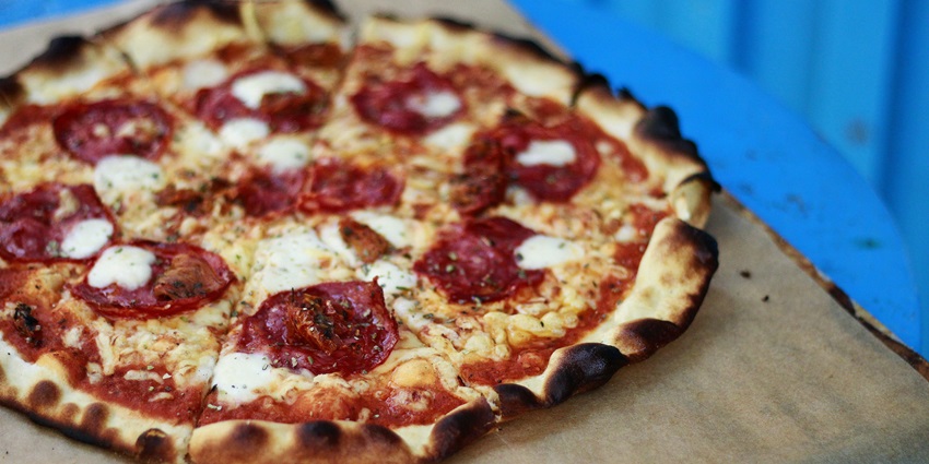 Plate of traditional Lithuanian pizza filled with meat, topped with sour cream and bacon.