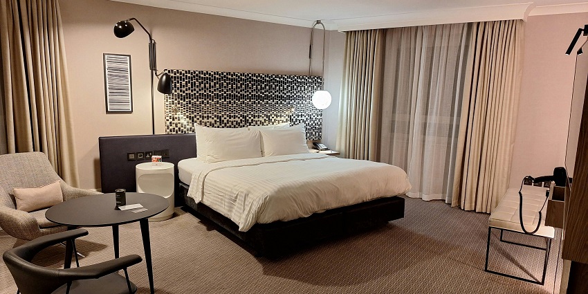 Interior of a hotel room with a neatly made bed, chairs and tables