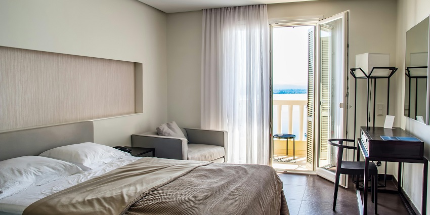 Interior of a hotel room with bed, mirror on the wall, sofa and lake from the balcony