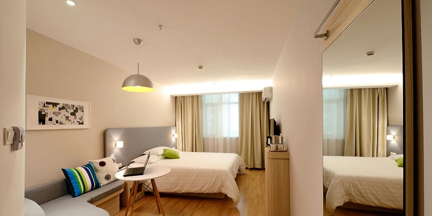 Modern hotel room with a cozy bed, sofa, wooden furniture, and warm lighting ambiance