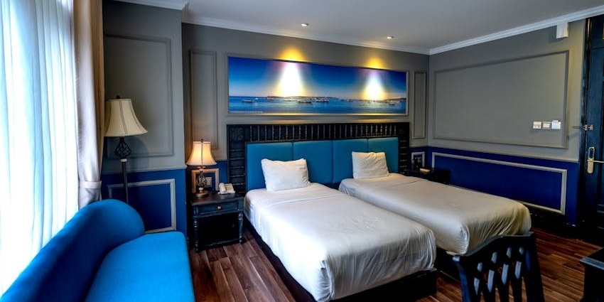 A hotel room with two twin beds, blue and gray walls, a large photo above the headboard