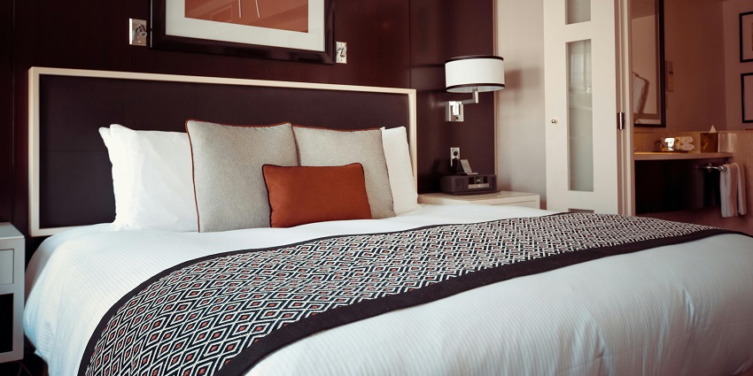 An image showing a black and grey bedspread on a bed with matching pillows in a hotel room.