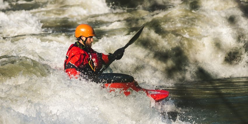 A man kayaking and navigating through intense whitewater rapids, battling strong currents.