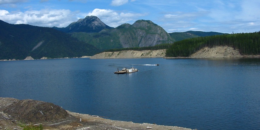 A peaceful lakeside view of Williston Lake, surrounded by green forests, one of the largest man-made lakes in the world.