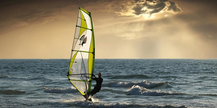 An image of a person windsurfing on the ocean with a green and white sail against blue sky