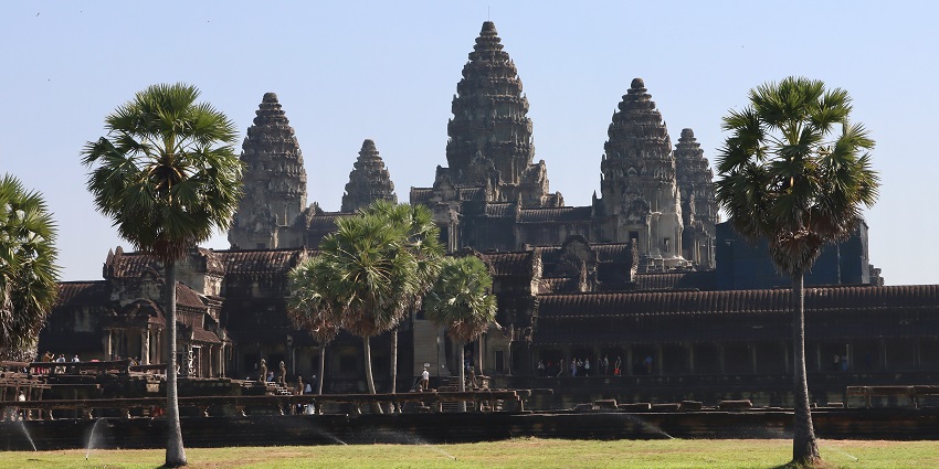 An image of Angkor Wat silhouetted against a radiant orange sunrise, with intricate towers and reflections.
