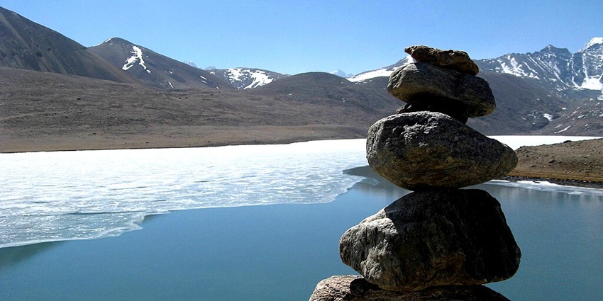 Stacked rocks with a jaw-dropping backdrop of partially frozen Gurudongmar Lake