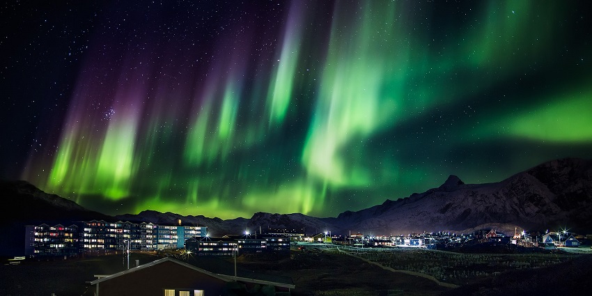A view of vibrant green and purple Northern Lights dancing above a mountain town.