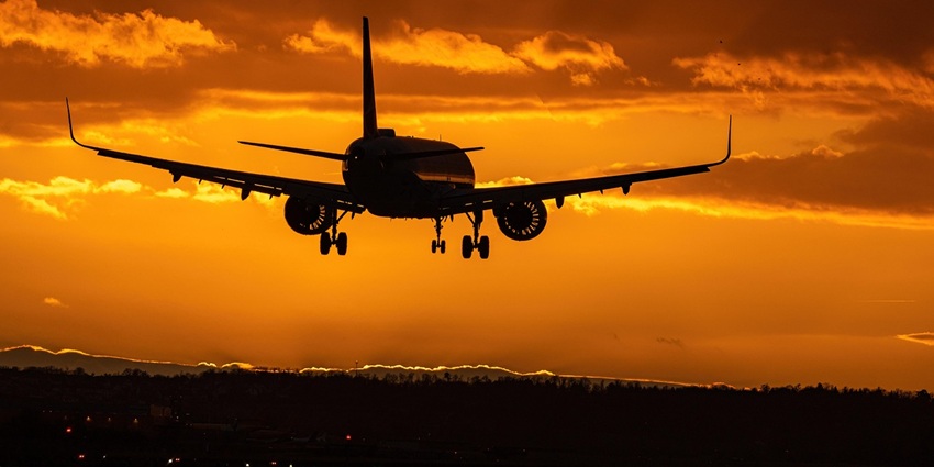 A flight takes off against an orange sky dotted with white clouds in the distance