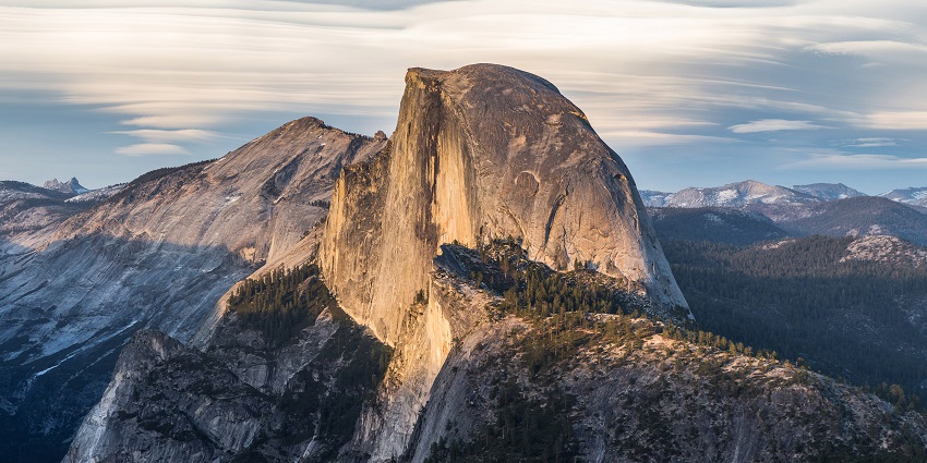 Yosemite's iconic Half Dome, its cliffs framed by mountains, forests, and clouds.