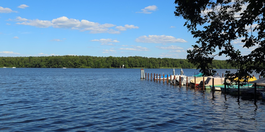 Zeuthen Lake with a large blue water body, multiple boats parked and distant greenery.