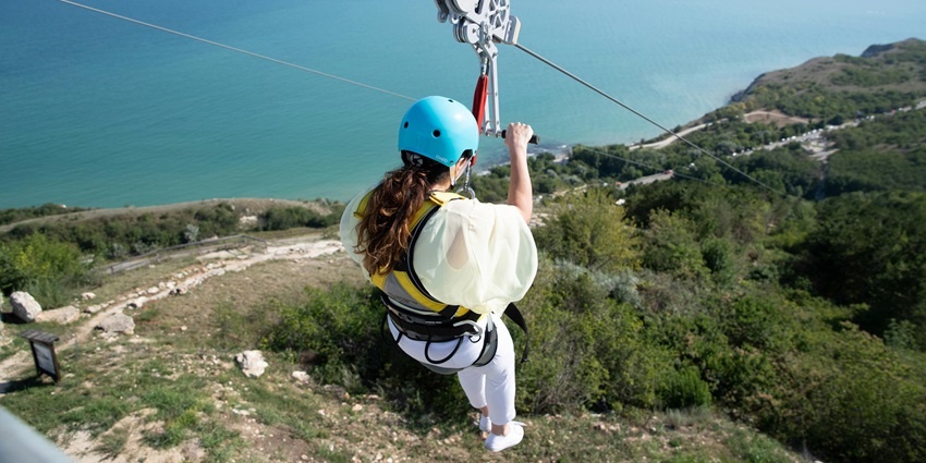 Tourist zip-lining with safety gear attached to his waist and helmet