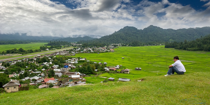 Ziro puto town from above with multiple traditional-style houses, greenery and a man sitting