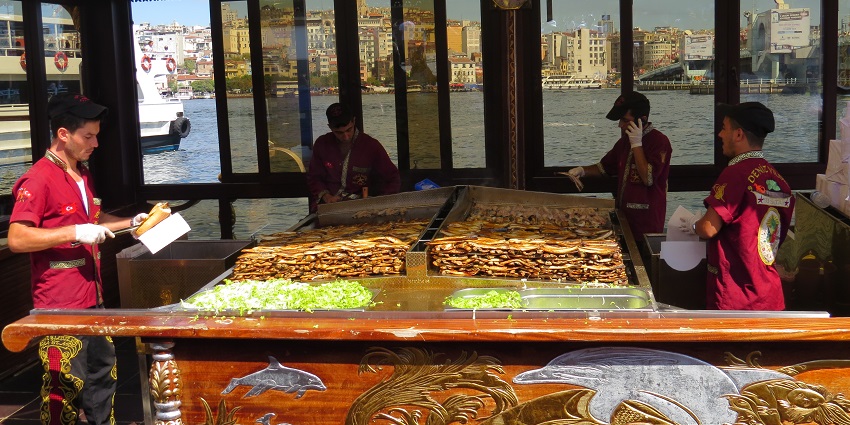 Balık Ekmek is being sold from a boat in Istanbul as four men in red shirts prepare and ready the food.