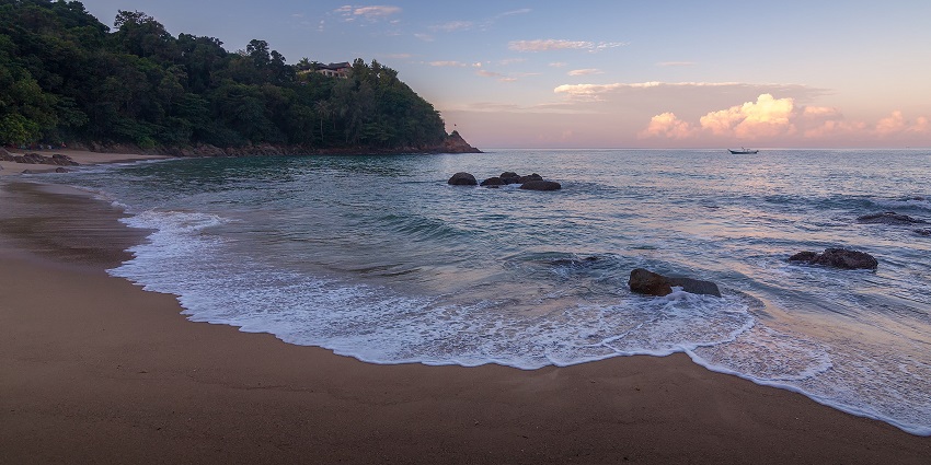A tranquil shot of Banana Beach in Phuket with clear blue waters, white sand, and gentle waves, one of the best places to visit in Phuket in October.
