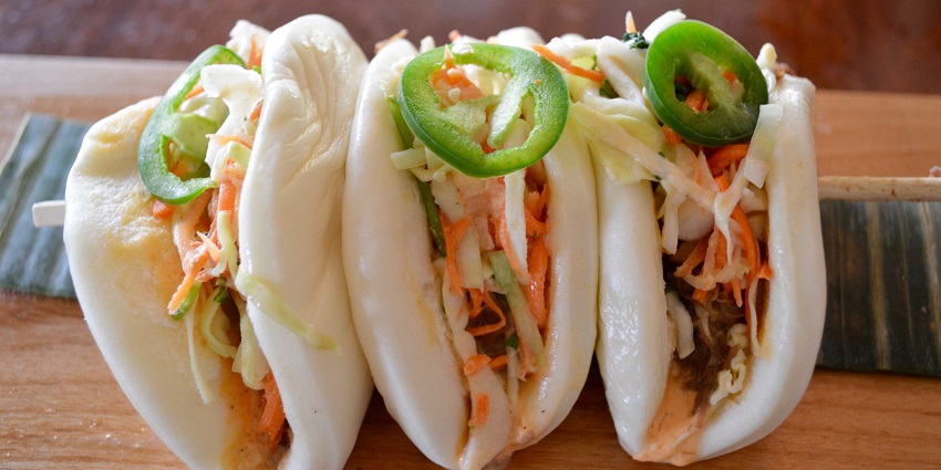 Steamed bao buns filled with tender meat, and fresh veggies, and garnished with herbs