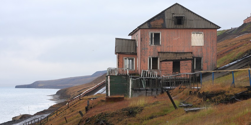 Barentsburg settlement with industrial buildings set against rugged Arctic terrain and cloudy sky.