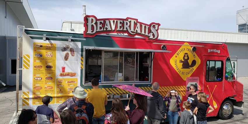 A group of people stand in front of a BeaverTails food truck near a museum in Toronto.