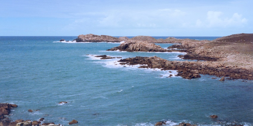 Rocky shoreline along Bryher’s west coast with rugged terrain and open sea under cloudy skies.