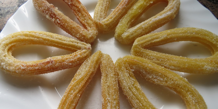 A glimpse of a flowery shape made of sugar-coated, delicious Churros on a plate.