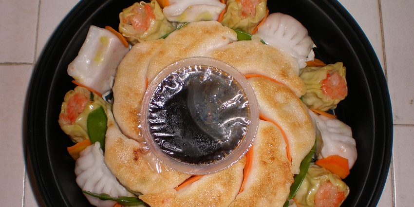 Dim sum platter featuring assorted dumplings served with a side of soy sauce for dipping