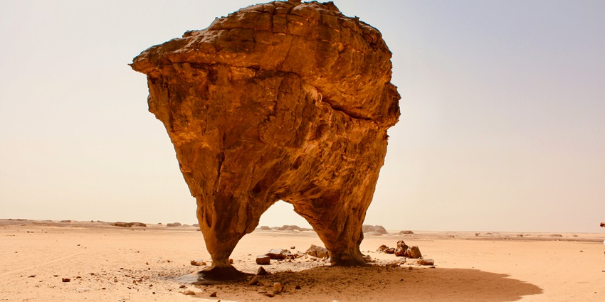 Large isolated rock formation in a sandy desert under a clear blue sky