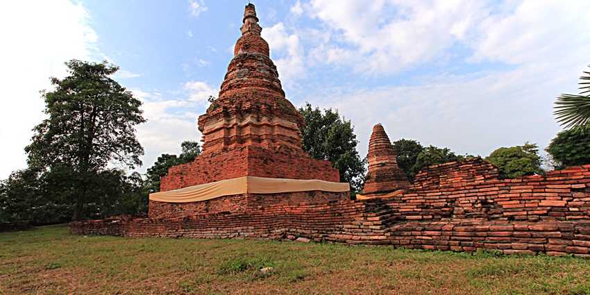 Open-air archaeological site with ancient brick foundations and a traditional Thai-style museum building in the background.