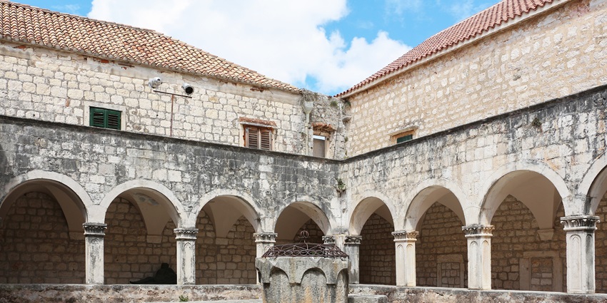 Peaceful inner courtyard of the Franciscan Monastery in Hvar with stone arches and columns, one of the best things to see in Hvar.