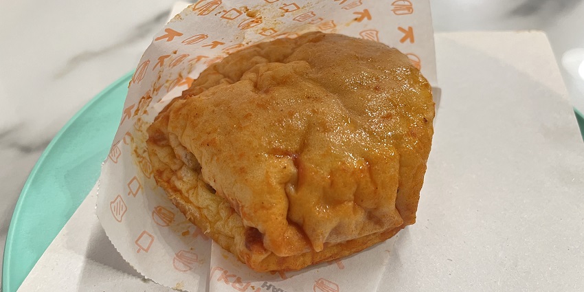 Wet meat burger served in a branded wrapping paper placed on a plate over a table
