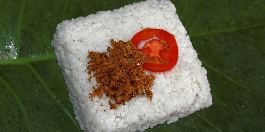 A plate of Kiribath with Lunu Miris, milk rice with spicy onion, sambal and tomato on top.
