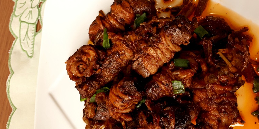 On a plate is Kokoreç served as long pieces in thick sauce and garnished with spring onions.