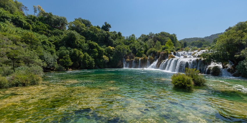 An image showing visitors swimming in Krka National Park, with waterfalls and natural surroundings.