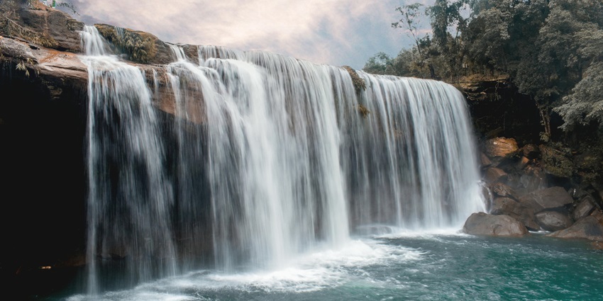 Scenic view of cascading Liduduhniap Twin Waterfalls surrounded by rocks and greenery under daylight.