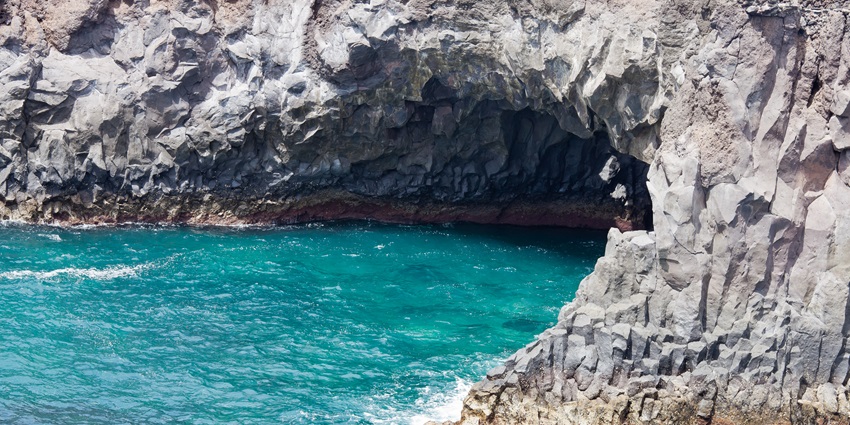 A picture of a cave system formed by volcanic rocks around a sea in Playa Blanca