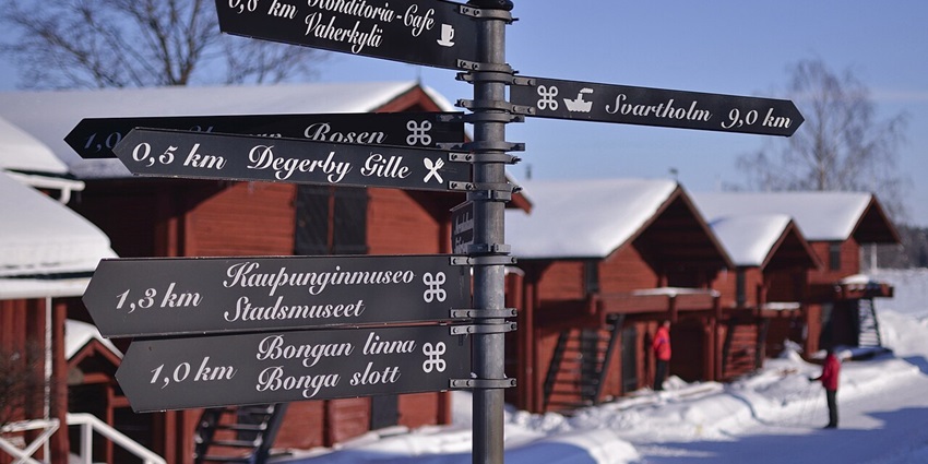 Snow-blanketed red wooden buildings in Loviisa’s old port during a crisp winter day.