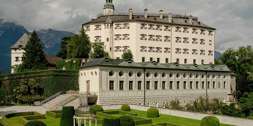 Snow-dusted Renaissance castle of Schloss Ambras with arched windows and a serene winter garden in the foreground.