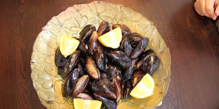 Slices of freshly prepared Midye Dolma served with four lime cuts on a brown plate.
