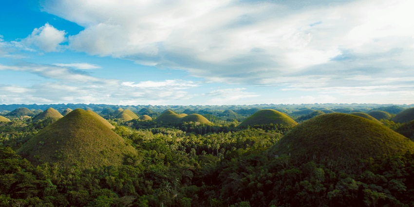 Rolling green hills blanketed with dense tropical forest under pastel sky.