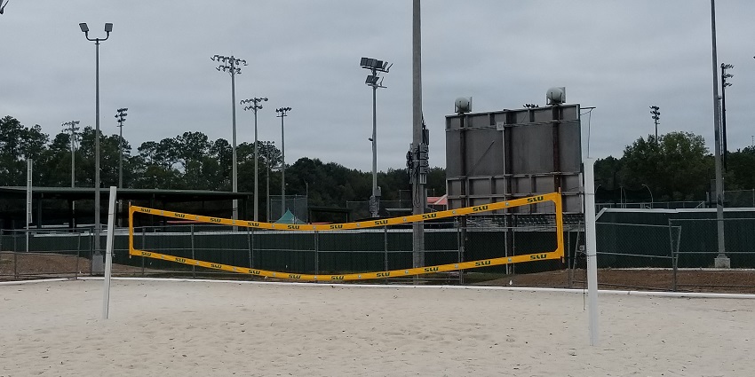 Beach volleyball court with players enjoying a game on the sandy shore under clear skies.