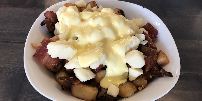 A plate of Poutine at a food stall, containing fresh bacon, sausages, and hollandaise sauce.