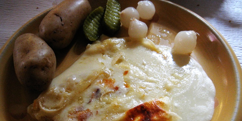 An image showing raclette, the best food in Switzerland, with melted cheese served over potatoes.