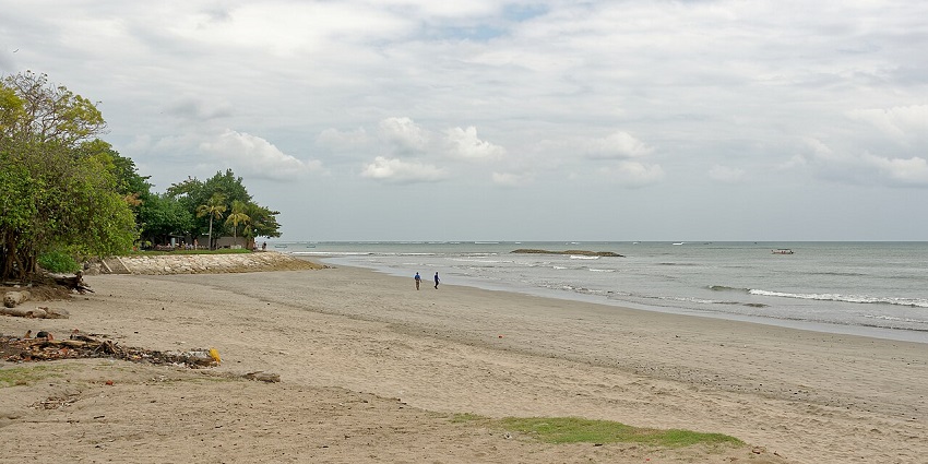 Golden sunset over Benua Patra Beach with gentle waves, rocky shoreline, and silhouettes of visitors enjoying the view, one of the bes things to see in Balikpapan.