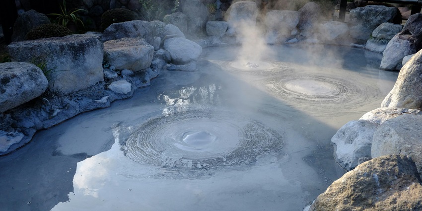 A hot spring in Luna Jaguar steaming in the sunlight, surrounded by rugged terrain.