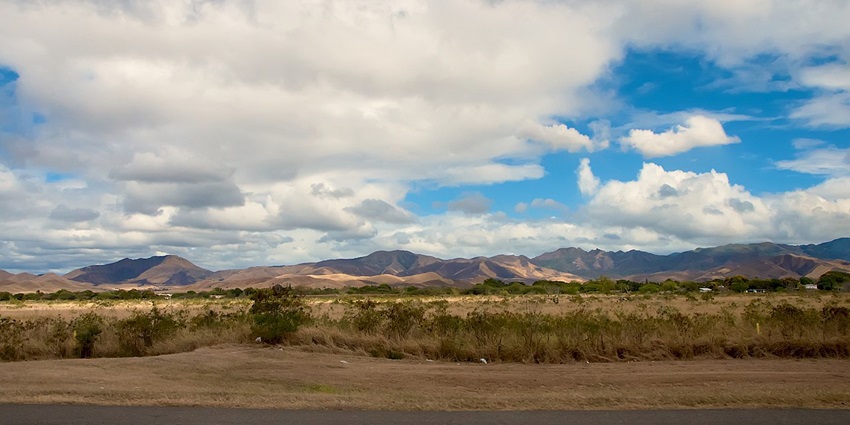 A deserted landscape under a bright cloudy sky, with a mountain range in background