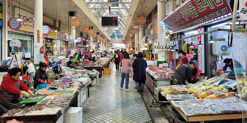 Colorful market stalls at Pasar Inpres Kebun Sayur displaying gemstone jewelry, batik fabrics, and traditional Dayak crafts under a covered walkway.