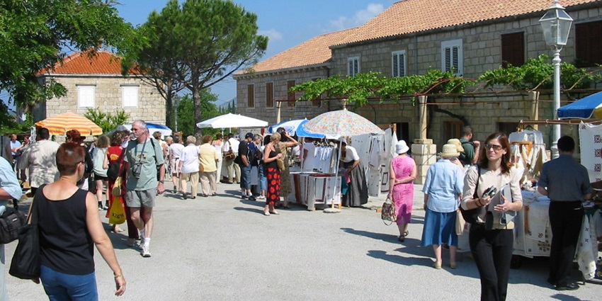 A picture of a local Croatian market in Dubrovnik with multiple stalls and numerous people buying stuff