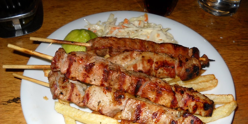 An image of Souvlaki, a grilled skewer dish eaten with soft pita bread, fresh salad, and a white sauce.