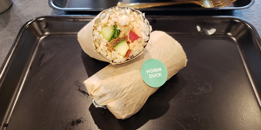 A pair of Sushi Burritos, cut in half, are served on a tray and are ready for takeaway.