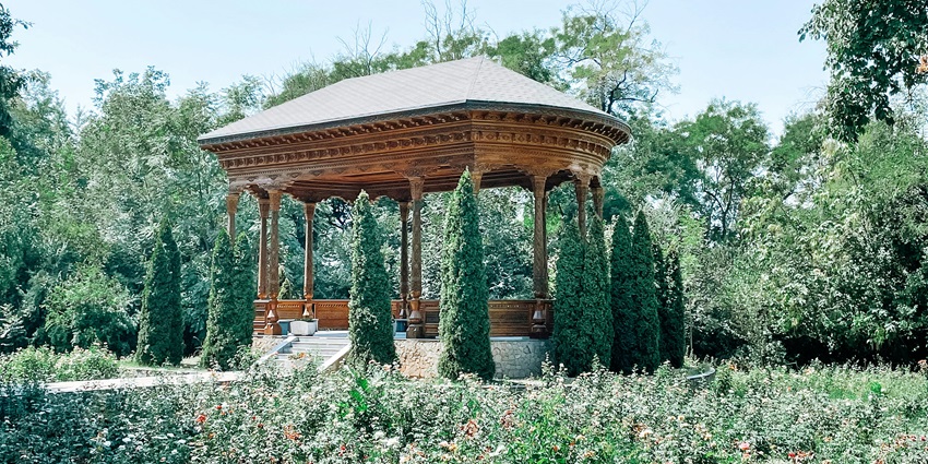 Wooden garden bower nestled amid lush greenery under a clear, bright sky–places to visit near china